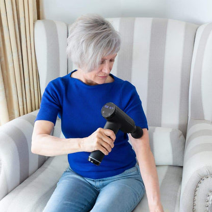 Woman in a chair massaging her elbow with the Massage Therapy Gun